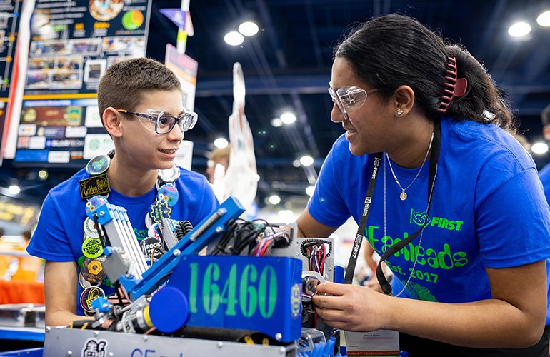 two students work on their robot between competition at a FIRST tournament.